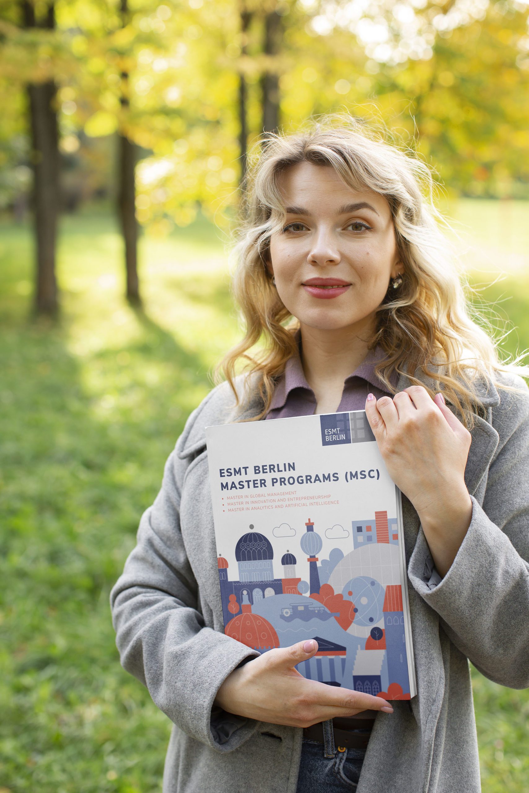 A student at ESMT Berlin posing with the ESMT Master Program prospectus outside the campus