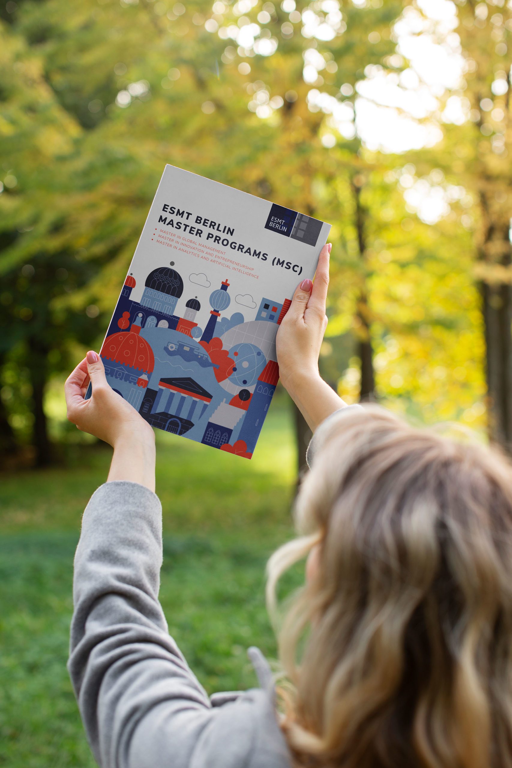 A student at ESMT Berlin holding up the ESMT Master Program prospectus outside the campus