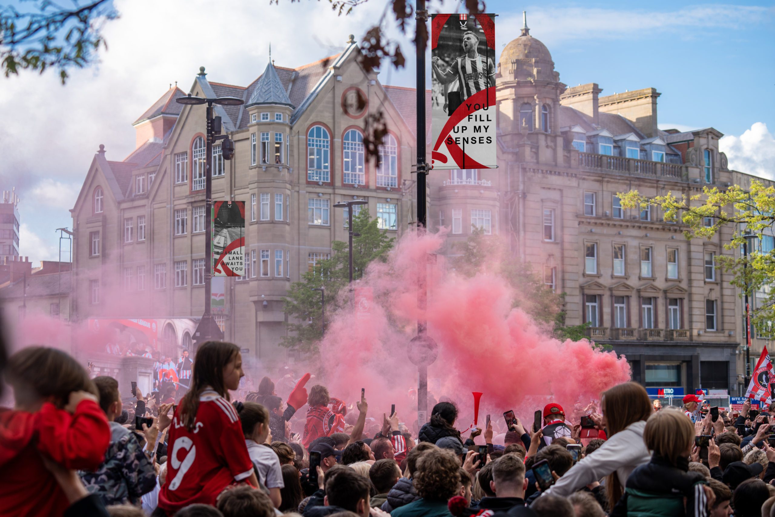 A crowd of fans celebrating Sheffield United getting promoted to the Premier League. In the background is two flags which PWF Studio created